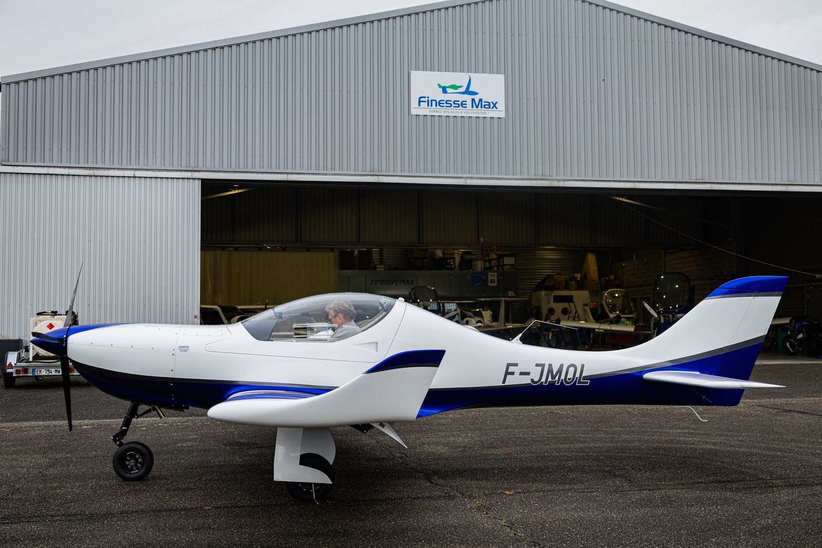 Aerospool Dynamic WT9 F-JMOL blanc et bleu à train rentrant, de profil devant le hangar Finesse Max