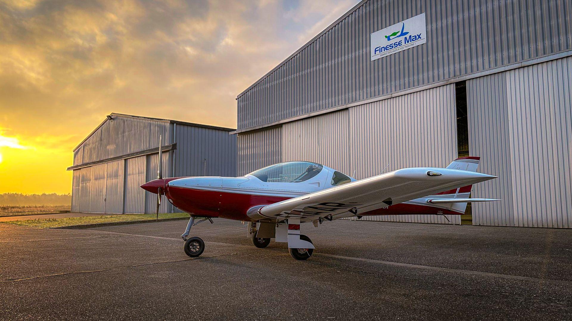 Avion léger devant un hangar au coucher du soleil