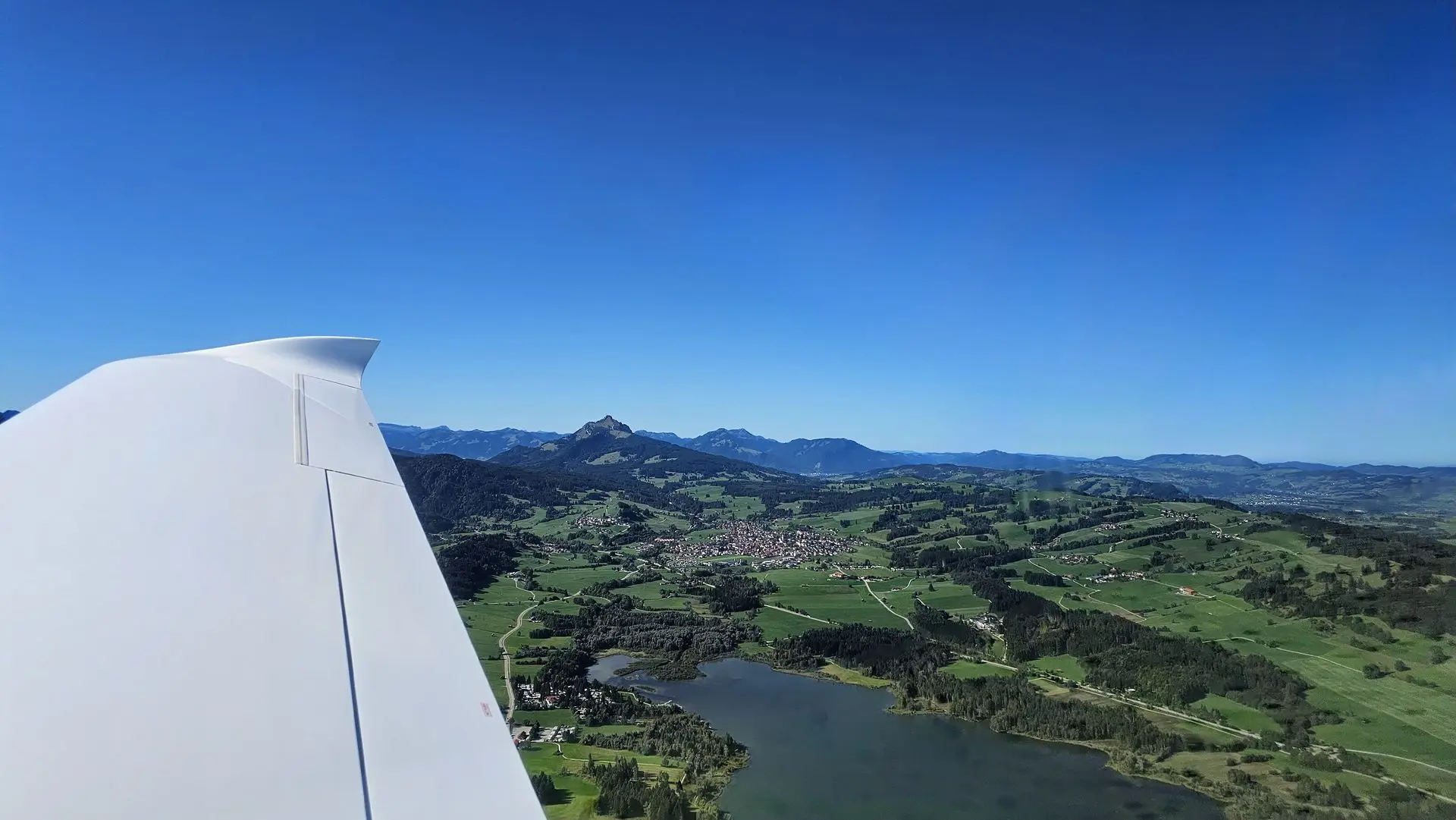 Vue depuis le cockpit : l’aile au-dessus d’un lac et des montagnes